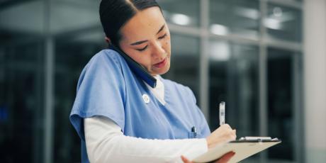 Krankenhauspersonal am Telefon mit Klemmbrett in der Hand