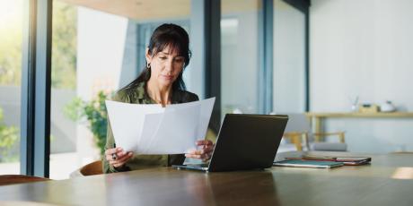 Frau am Tisch mit Laptop und Papieren
